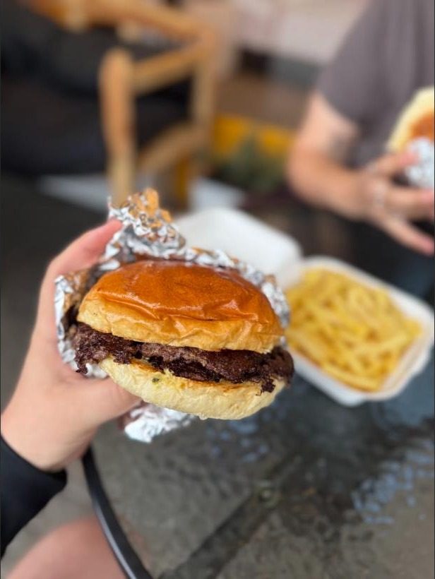 Burger Oklahoma trzymany w dłoni, w tle frytki